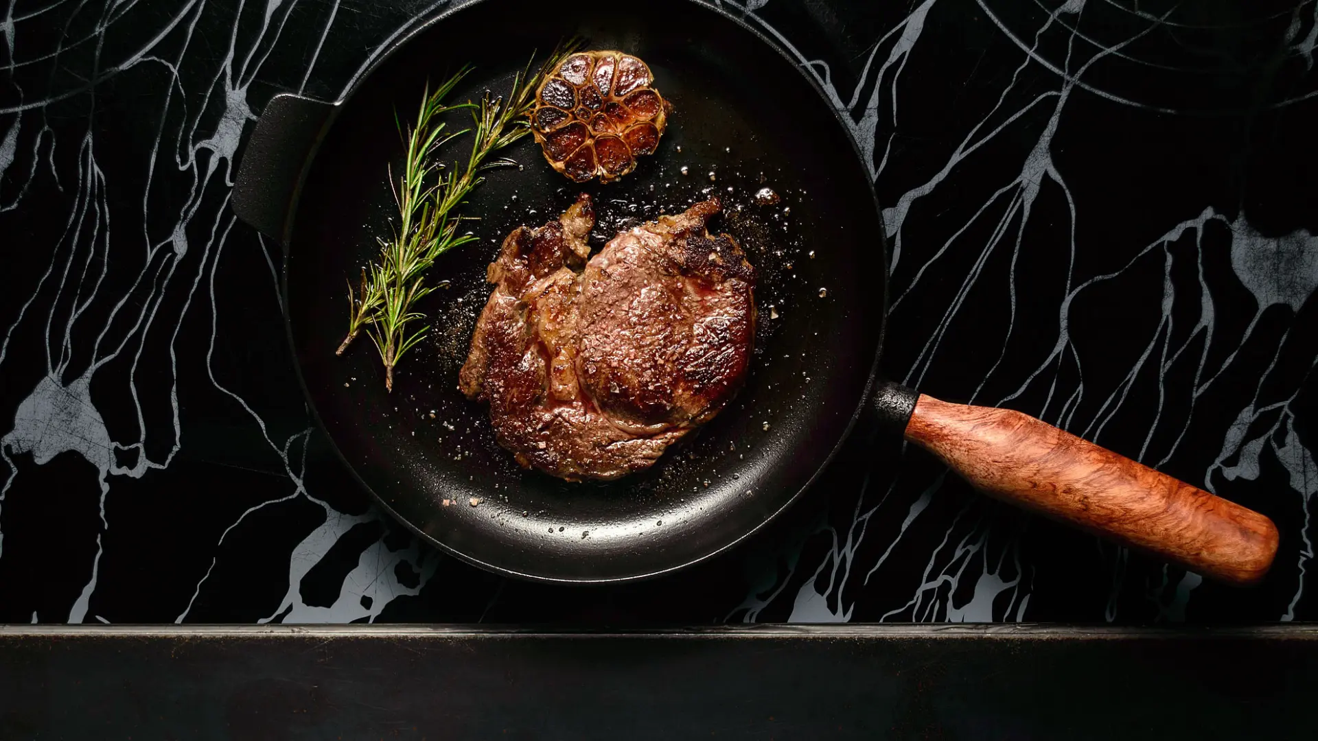 Ribeye-Steak mit Rosmarin und Knoblauch brutzelt in der gusseisernen Bratpfanne