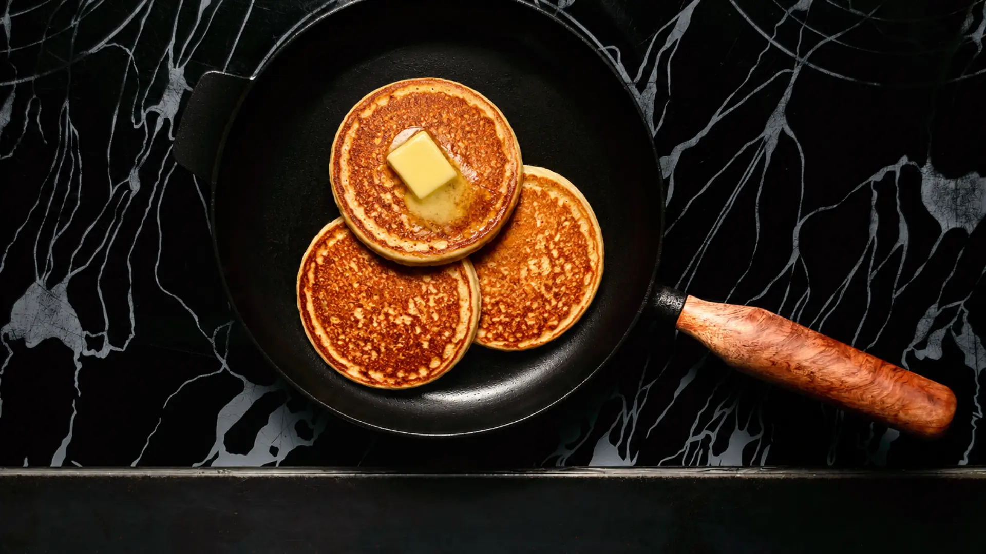 Drei goldbraune Pancakes mit Butter in der gusseisernen Bratpfanne